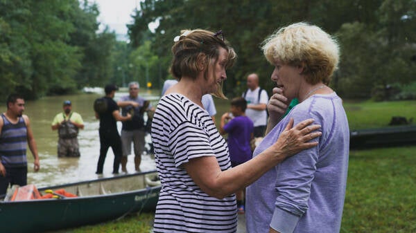 A woman consoling another woman in front of many individuals in a flooded area